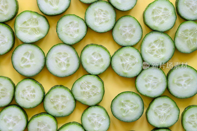 黄色背景上的黄瓜(Cucumis sativus)切片的全帧图像，显示绿色的皮肤和白色的果肉与白色的种子，健康饮食海报壁纸背景设计，高架视图